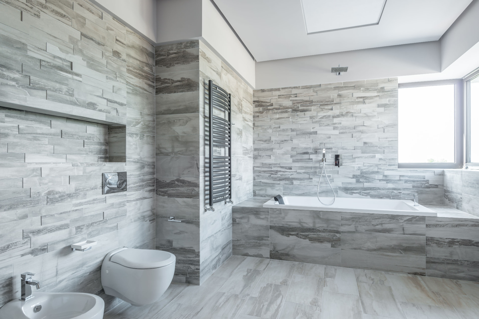 Grey stacked-stone and large-format tile bathroom with floating toilet and built-in soaking tub, Upland California